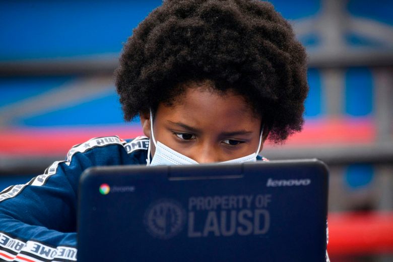 A child wearing a face mask looks at a laptop computer.