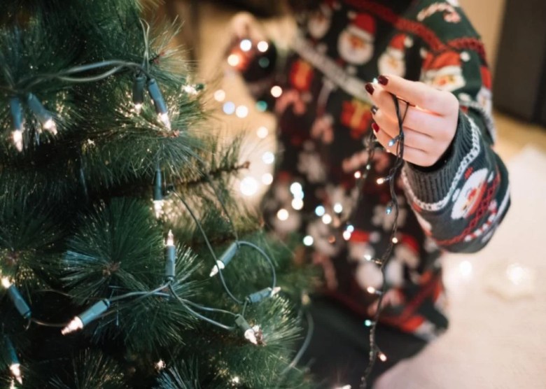 Electric lights, candles, and oil lamps A woman putting lights on a Christmas tree.